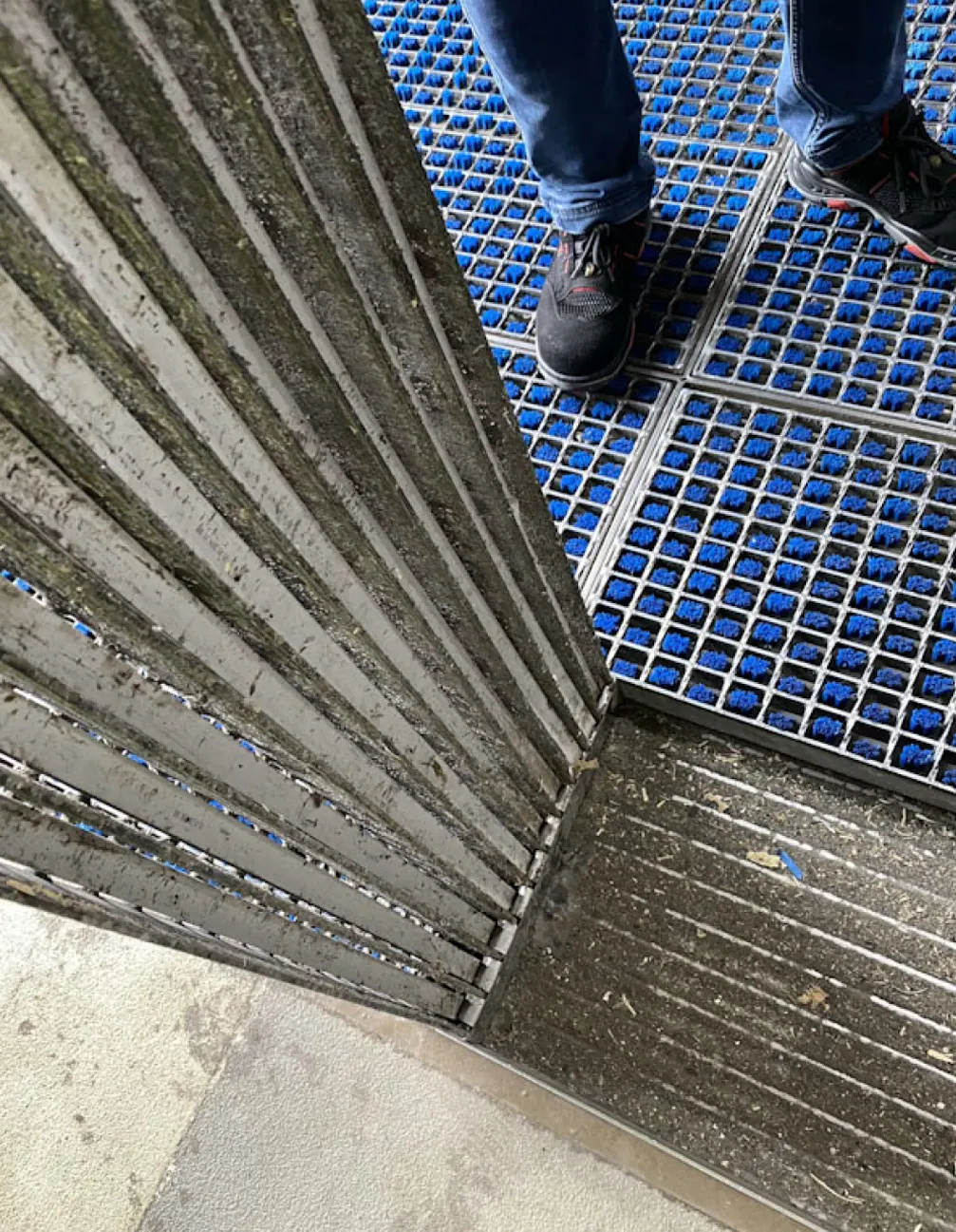 Detalhe das escovas metálicas do sistema ProfilGate® instaladas no piso da fábrica, com uma pessoa passando por cima
