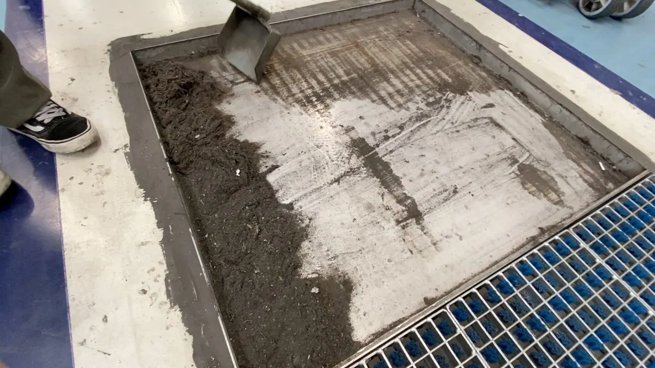 Sujeira preta recolhida do chão da fábrica sendo pesada numa balança, ao lado da grade do ProfilGate®